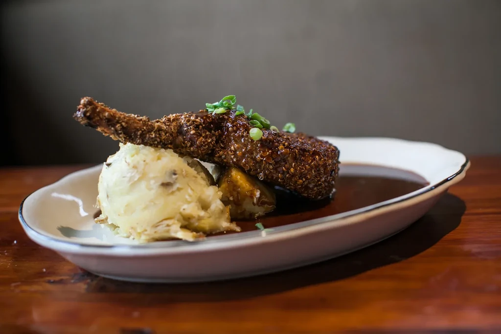 Crispy quinoa-crusted bone-in chop on mashed potatoes with rich dark sauce.