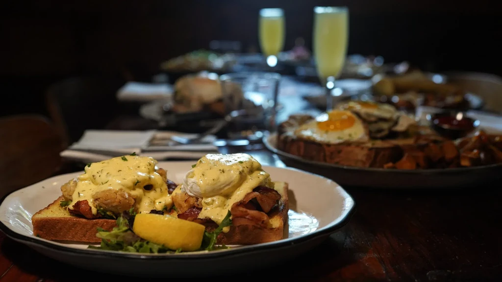 Close-up of Eggs Benedict and mimosas on a blurred restaurant table.