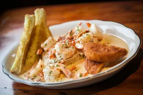Close-up of creamy shrimp seafood with herbs, toast, and fritters.