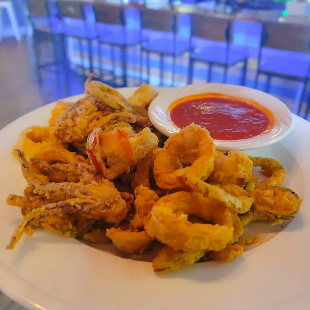 Crispy fried seafood and vegetables with red sauce on a white plate.