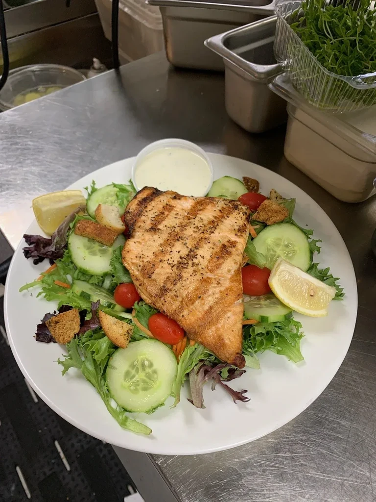 Grilled salmon salad with mixed greens, lemon, and dressing in a kitchen.