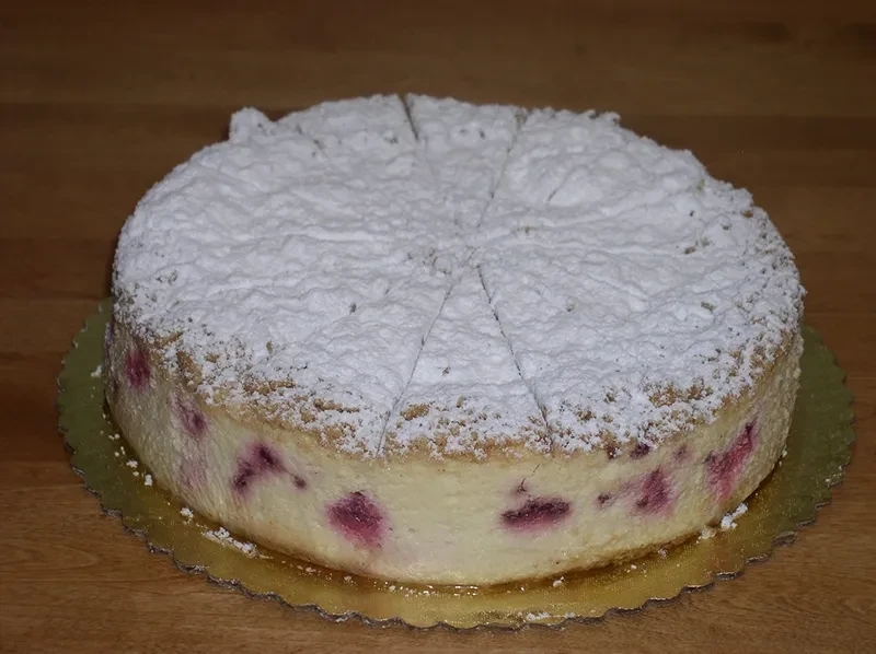 Creamy berry cake topped with powdered sugar, sliced on a golden board.