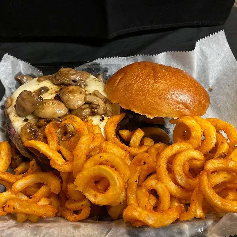 Open-faced burger with melted cheese, mushrooms, and crispy curly fries.