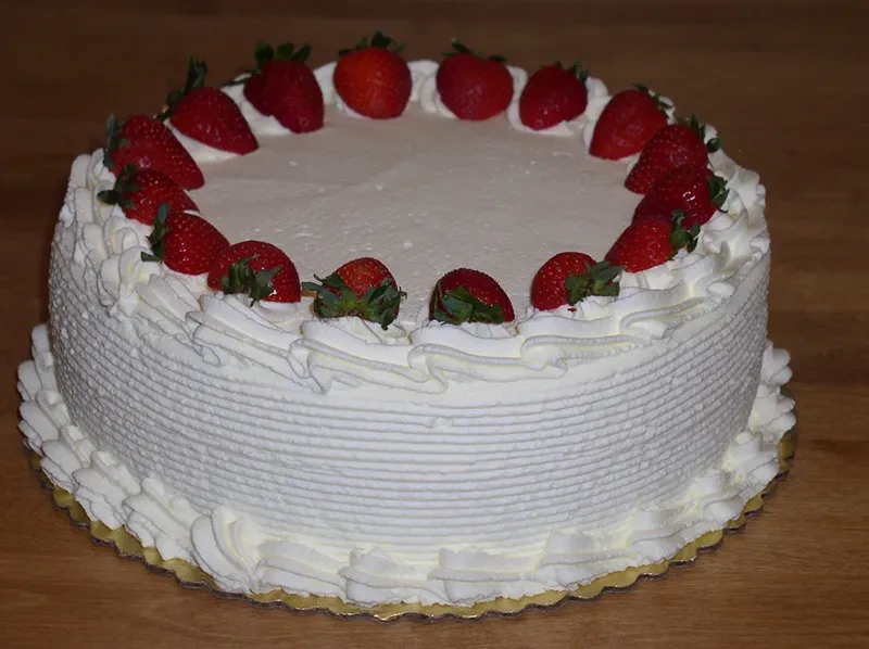 Round white cake with decorative frosting and a ring of fresh strawberries.