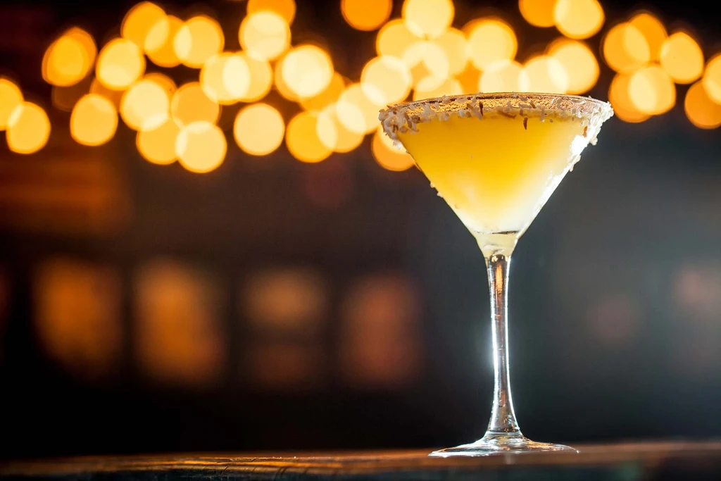Yellow, sugar-rimmed cocktail in a martini glass on a dark bar.