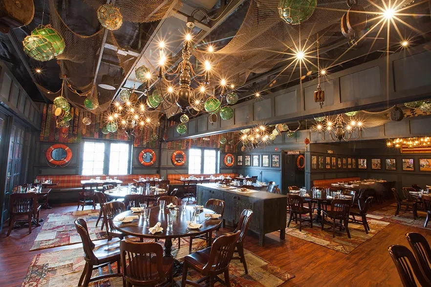 Nautical-themed restaurant interior with empty tables, fishing nets, and glass floats.