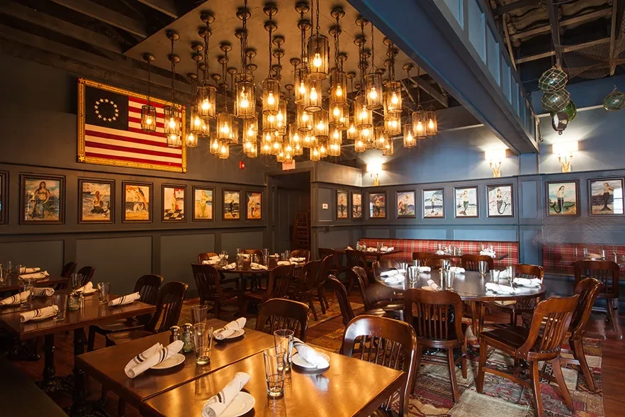 Restaurant dining room with industrial lights, mermaid art, and Betsy Ross flag.