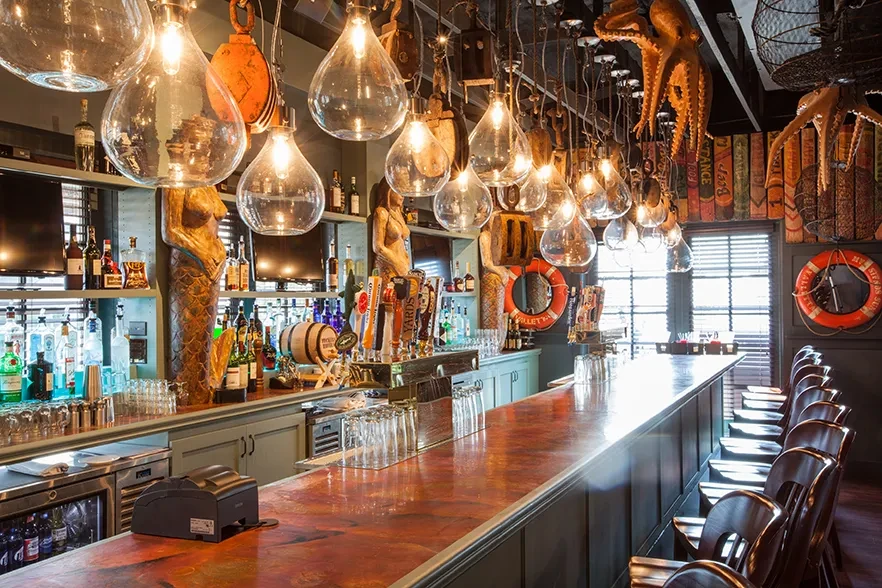 Warmly lit, nautical-themed bar with mermaids, octopuses, and a long counter.