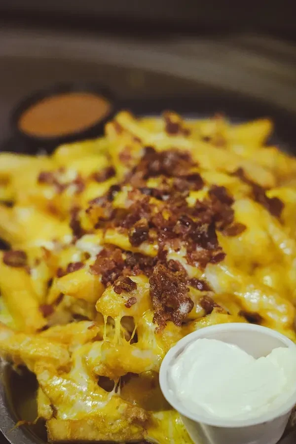 French fries with melted yellow cheese, crispy bacon, and white dipping sauce.