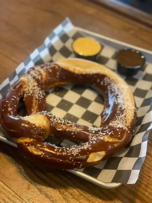 Dark brown salted pretzel, mustard and brown dips, checkered paper.
