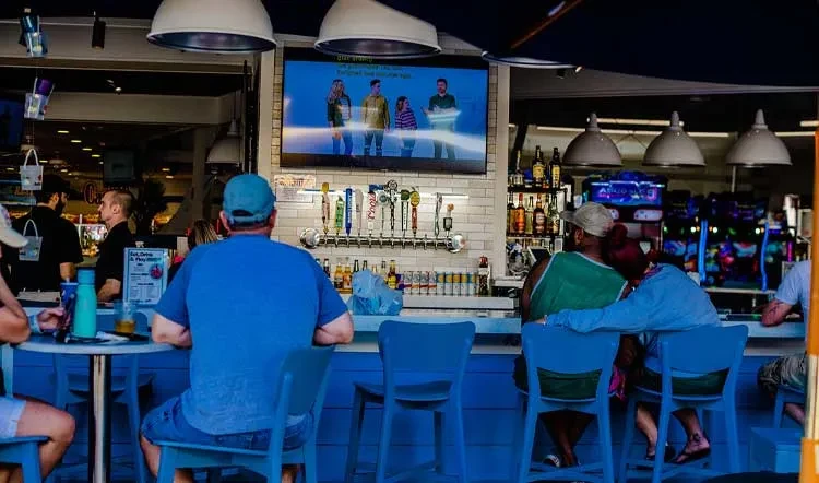 Bar with blue stools, patrons, beer taps, and a large TV.