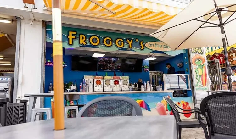 Froggy's on the pier shop: Blue counter, slushie machines, cartoon frog.