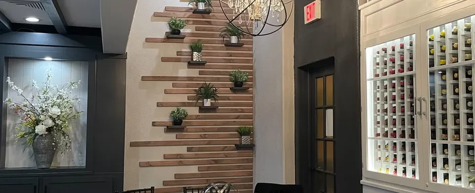 Elegant interior with floral display, wood wall, wine rack, and chandelier.