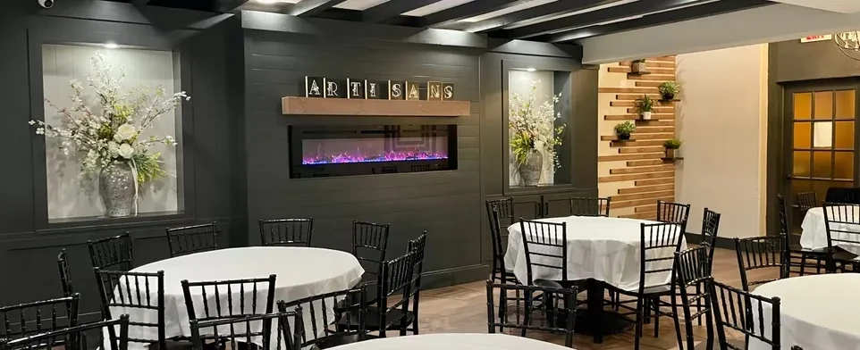 Empty dining room with tables, fireplace, floral arrangements, and "ARTISANS" sign.