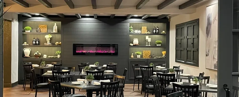 Restaurant interior features dark paneling, pink-purple electric fireplace, and dining tables.
