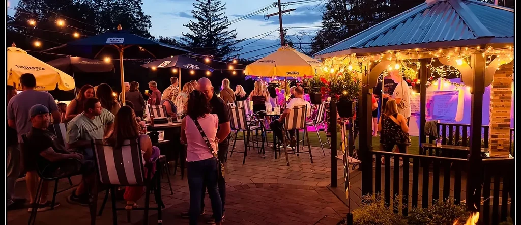Lively outdoor patio at dusk with patrons, string lights, and gazebo.