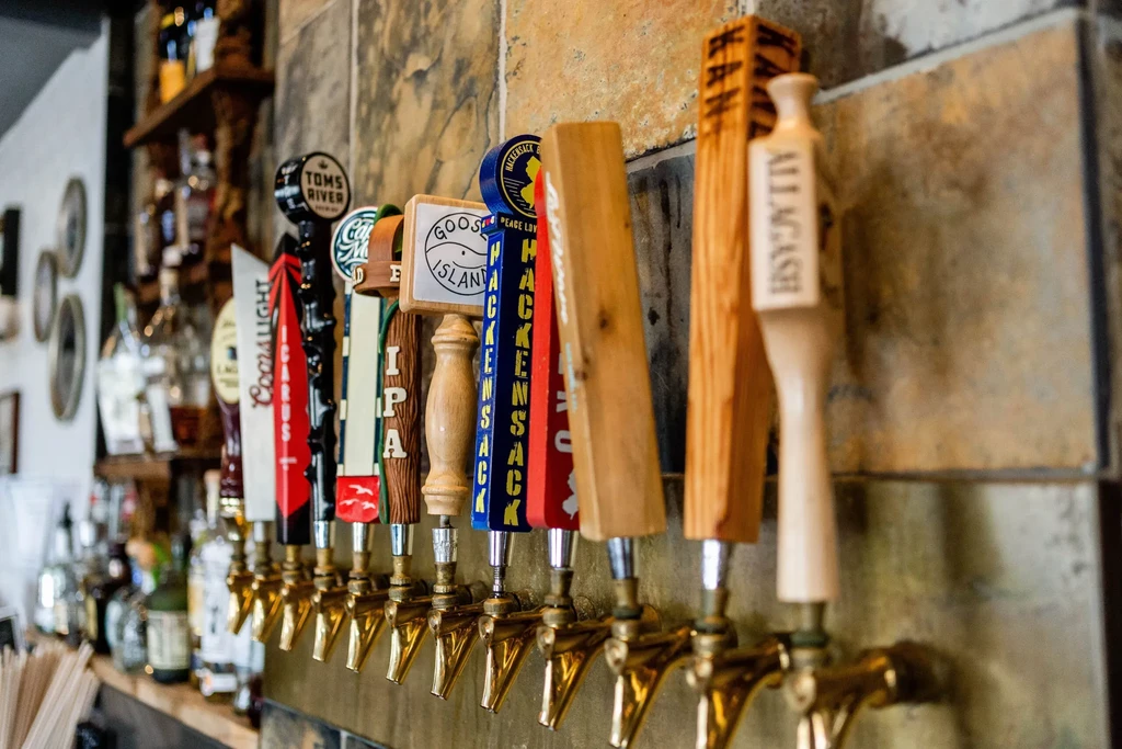 Close-up of a dozen unique branded beer tap handles at a bar.