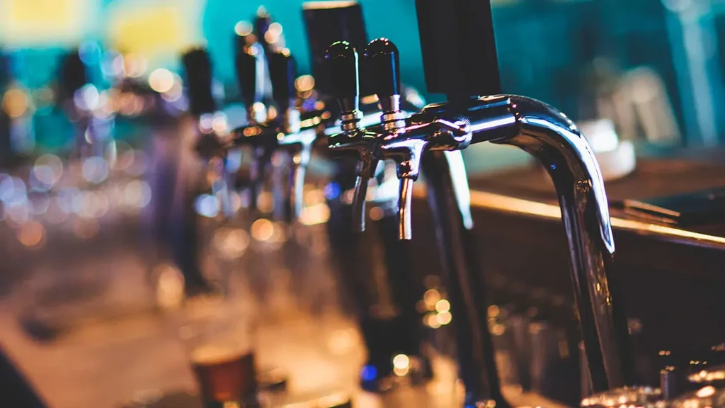 Close-up of a row of chrome beer taps in a blurred bar.