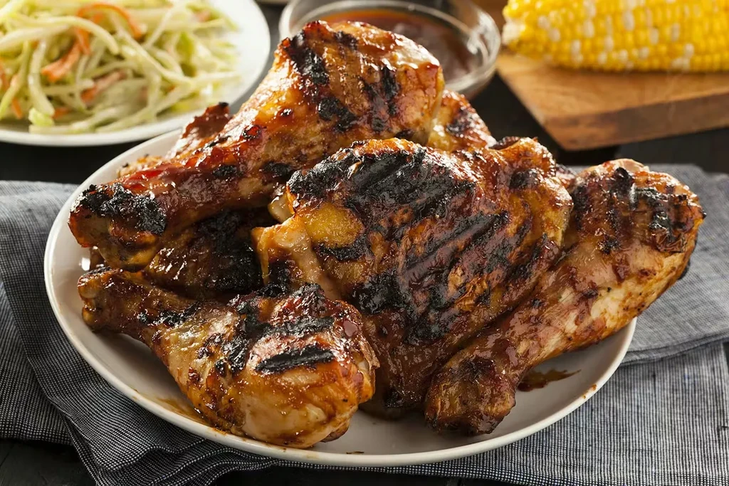 Grilled chicken drumsticks and thighs with coleslaw and grilled corn.