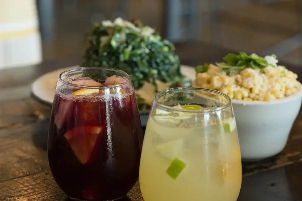 Two glasses of fruit drinks and two food dishes on a rustic table.