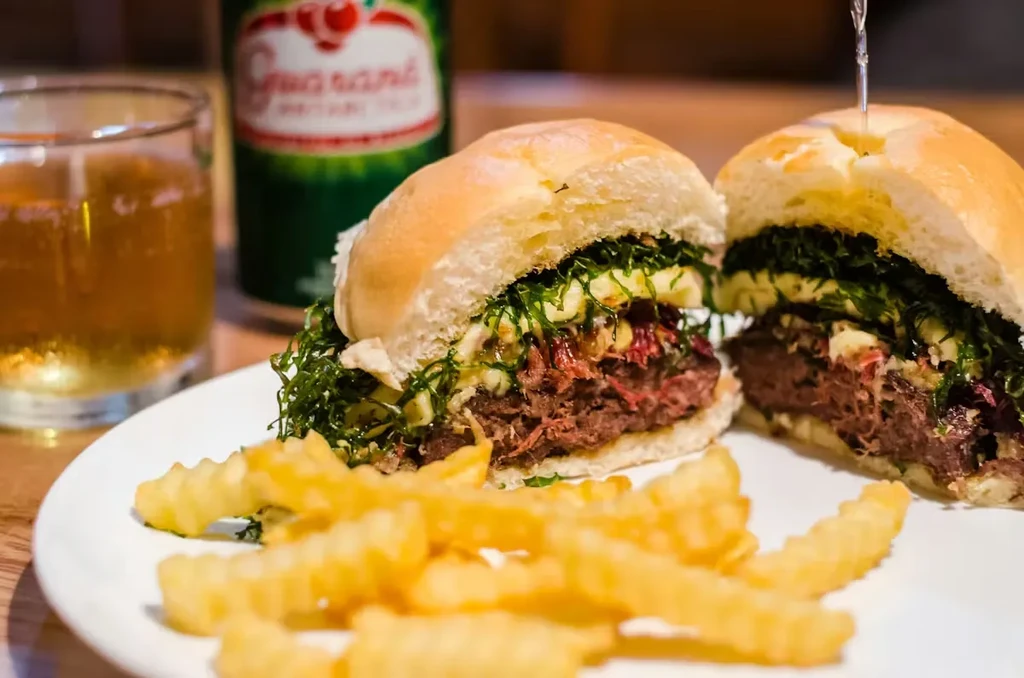 Halved shredded meat sandwich with greens, fries, and soda.