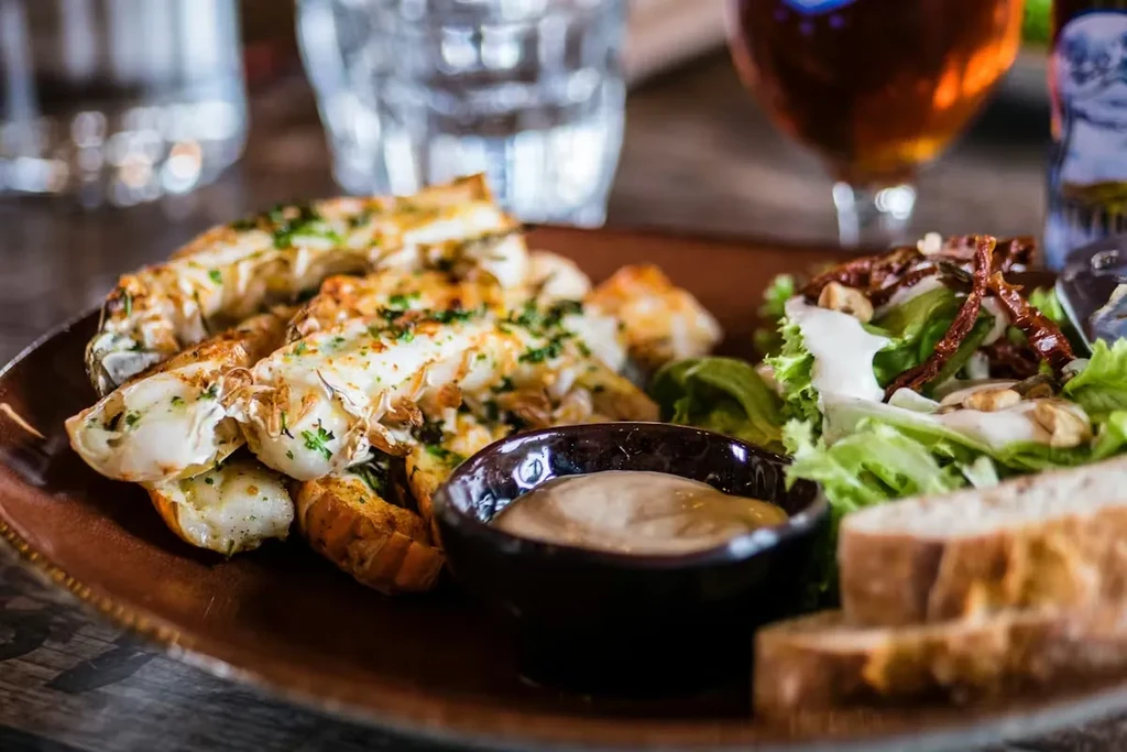 Grilled lobster tails, fresh salad with nuts, artisanal bread, and creamy sauce.