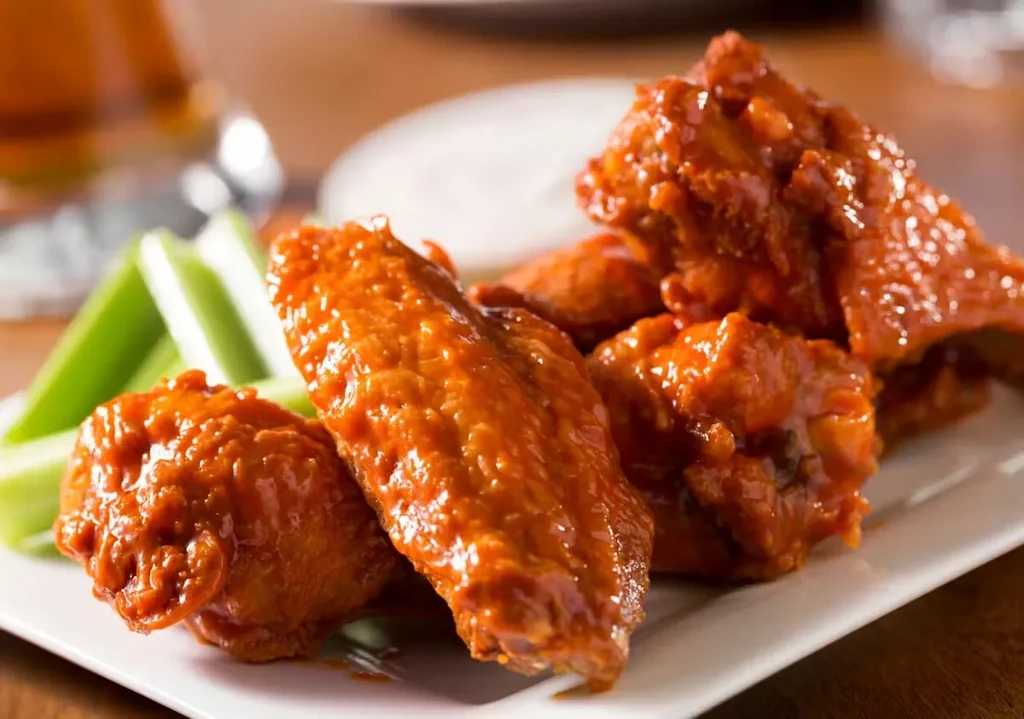 Plate of glossy orange-red buffalo wings with celery and dip.