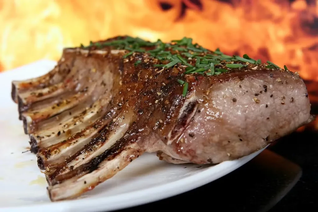Glistening, herb-topped rack of ribs on a plate with blurred flames.