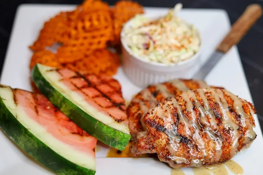 Plated grilled meat, grilled watermelon, sweet potato fries, and creamy coleslaw.