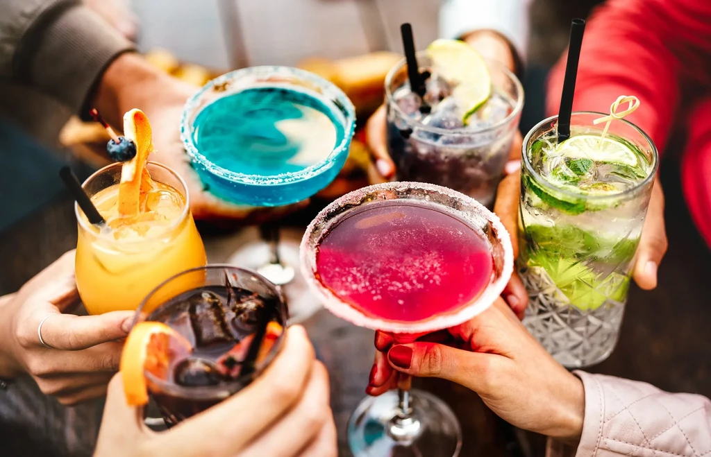 Diverse hands hold various colorful cocktails, toasting together.
