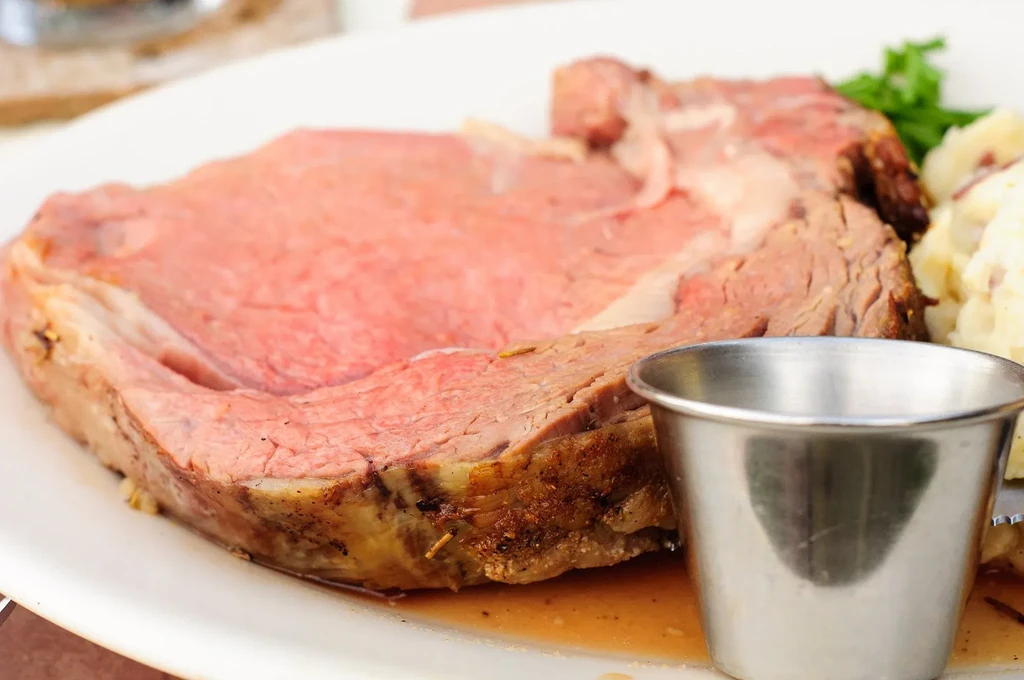 Medium-rare prime rib slice with au jus, sauce cup, and mashed potatoes.