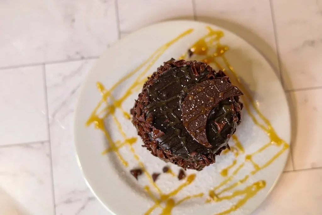 Dark chocolate dessert, glazed, with chocolate shavings, bark, and caramel drizzle.