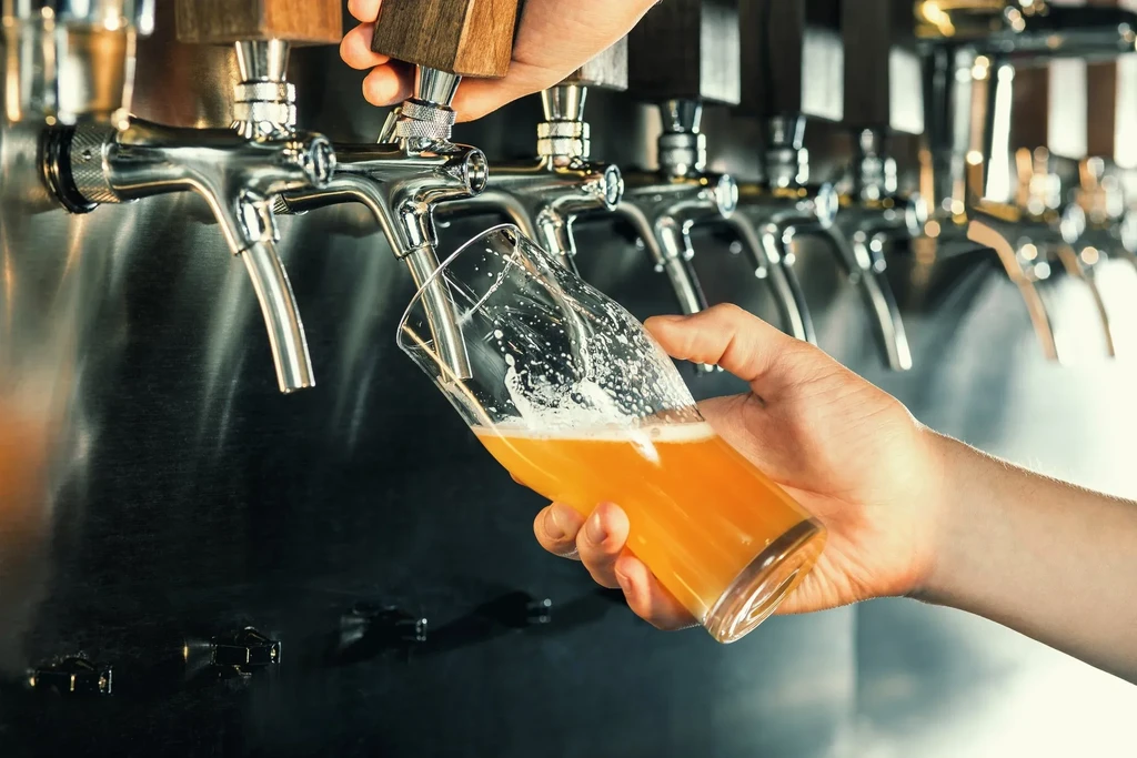 Hand pouring golden, frothy beer from a tap into a glass.