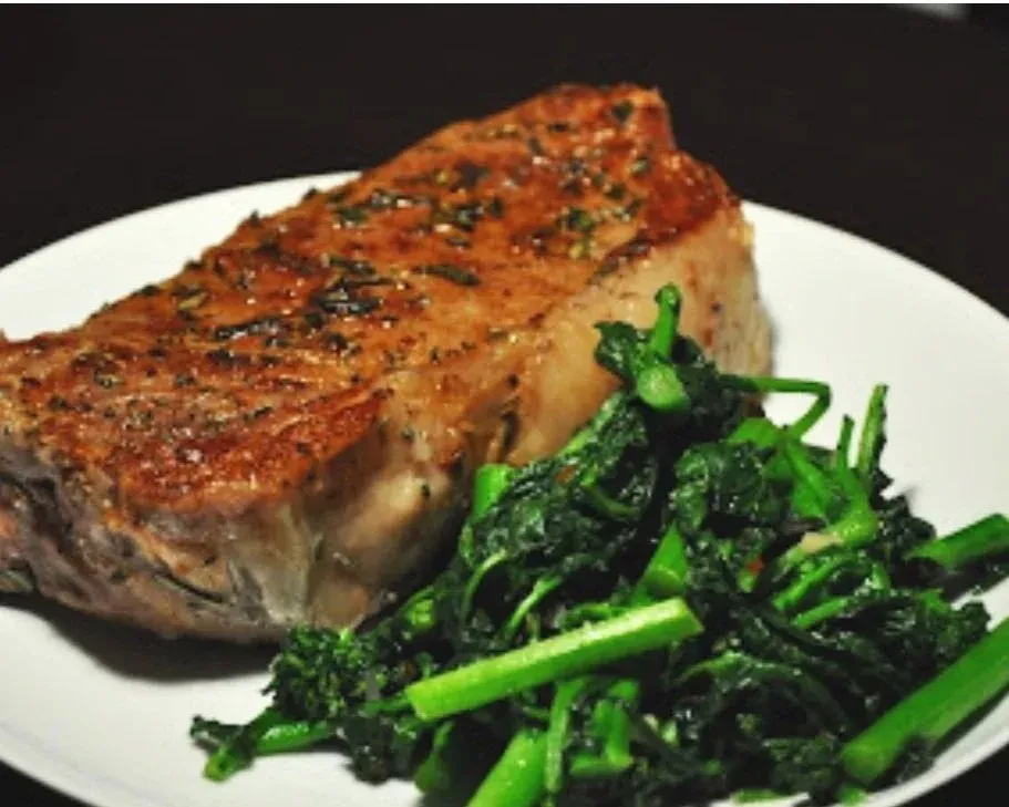 Thick-cut steak with herbs and vibrant green sautéed vegetables on a plate.