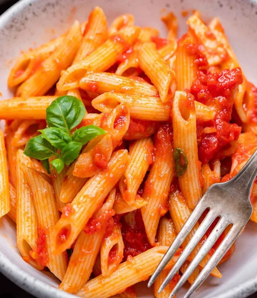 Penne pasta with chunky tomato sauce, fresh basil, and a fork.