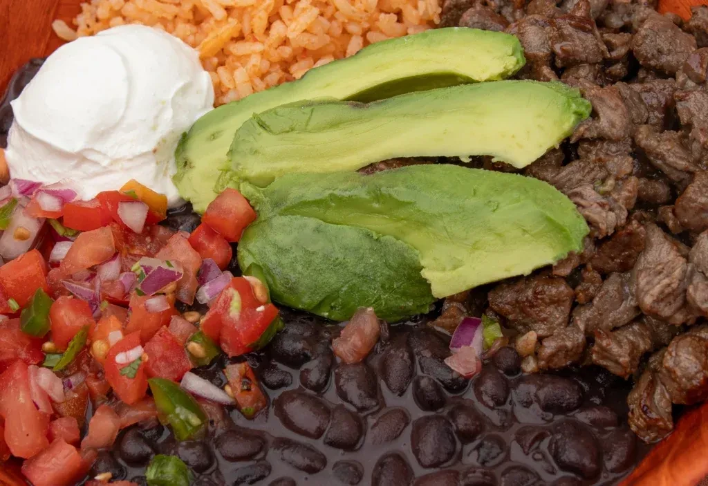 Vibrant Mexican bowl with rice, beans, meat, avocado, pico de gallo.