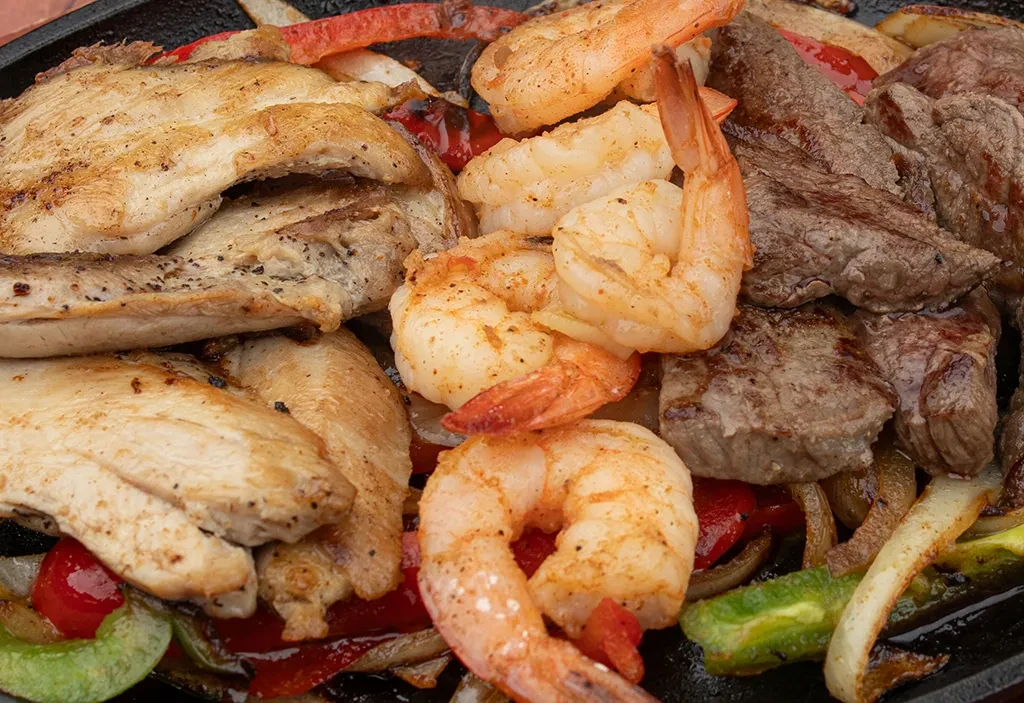 Sizzling chicken, beef, shrimp fajitas on a cast-iron skillet.