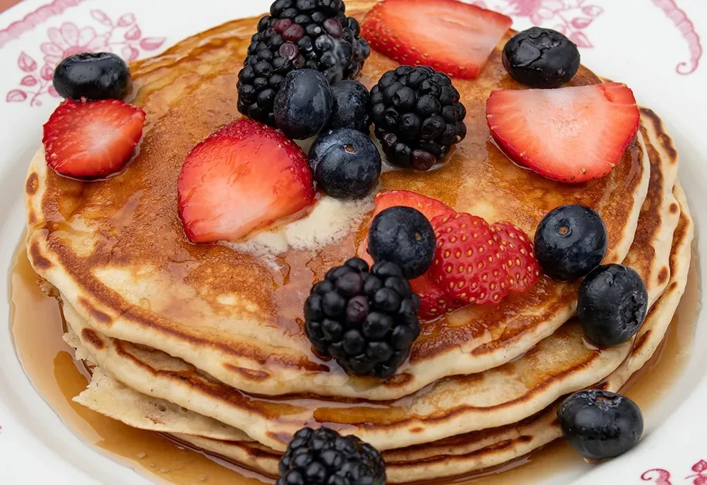 Pancakes with maple syrup, strawberries, blueberries, blackberries, and melted butter.