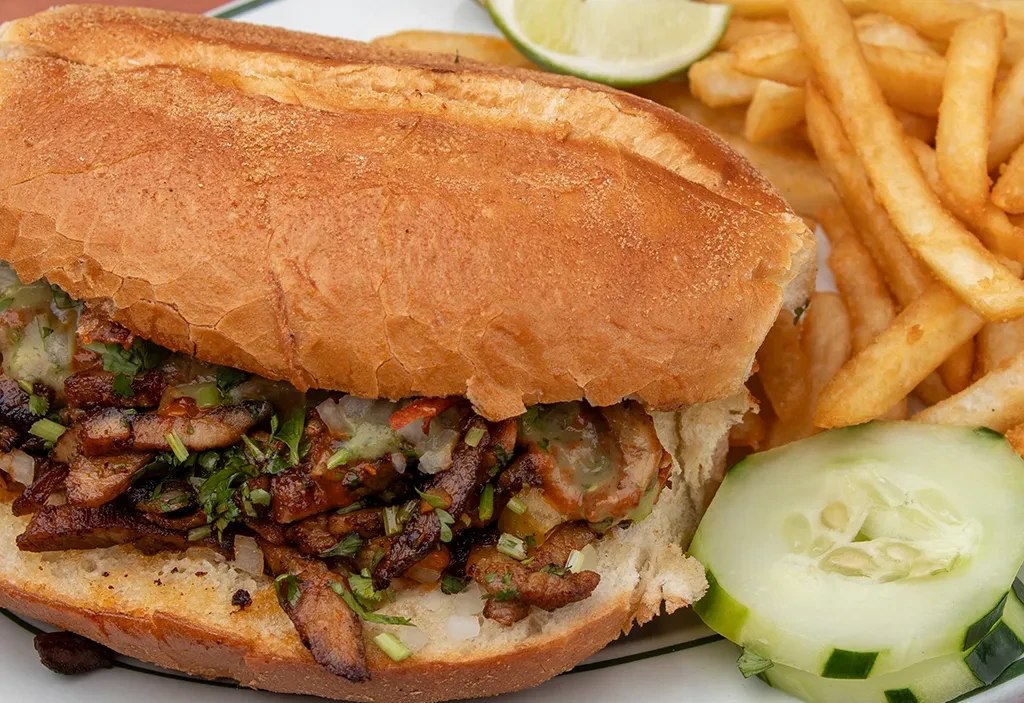 Large meat sandwich, cut open, with fries, lime, cucumber.