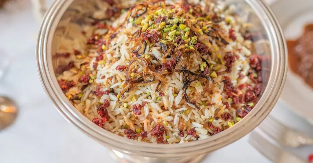 Ornate silver bowl of rice garnished with onions, pistachios, and barberries.