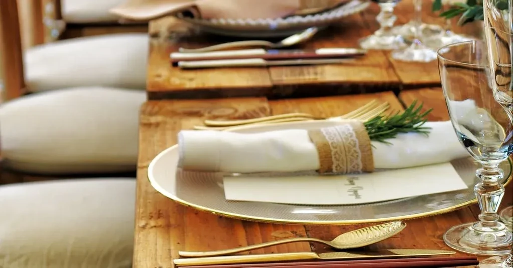 Elegant rustic table setting with rosemary, gold cutlery, and wine glasses.