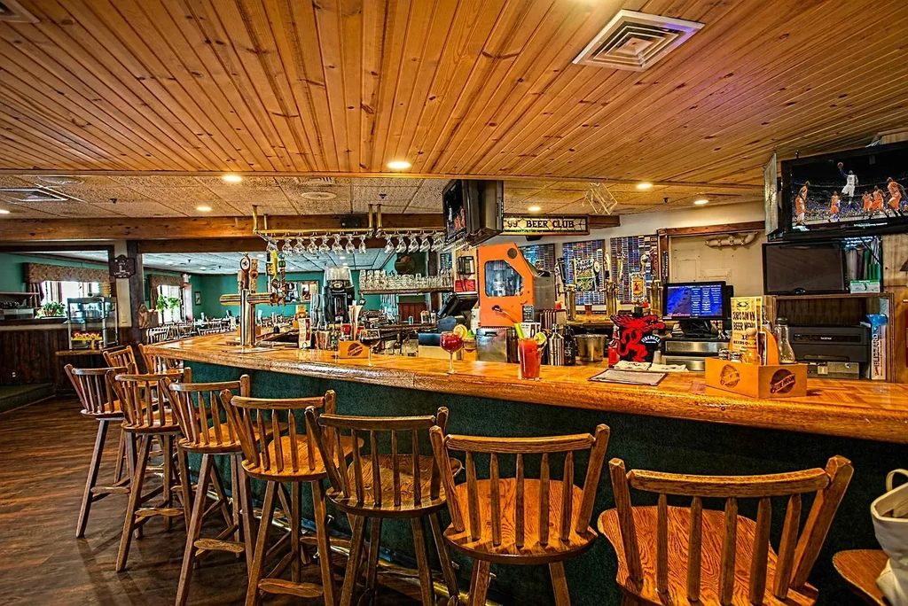 Curved wooden bar with green base, taps, cocktails, and a basketball game.
