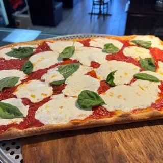 Rectangular pizza with red sauce, melted mozzarella, and green basil.