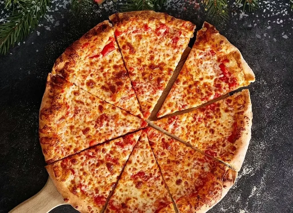 Overhead: freshly baked, sliced cheese pizza on peel with pine needles.