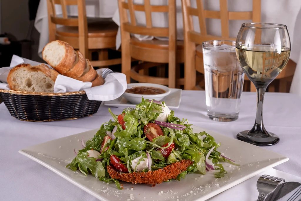 White plate with salad and breaded cutlet, bread, water, and wine.