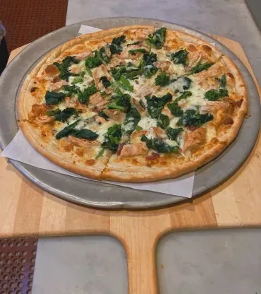 Freshly baked chicken and green vegetable pizza on a wooden peel.