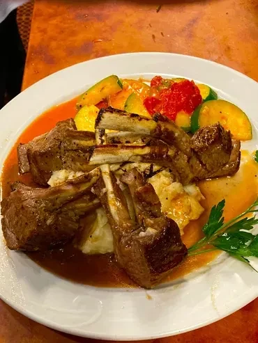 Top-down view of plated lamb chops, mashed potatoes, vegetables, and sauce.