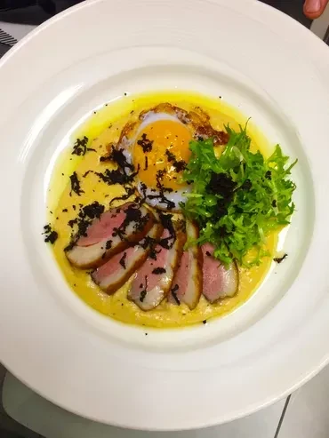 Artfully plated rare meat, fried egg, greens, sauce, and dark sprinkles.