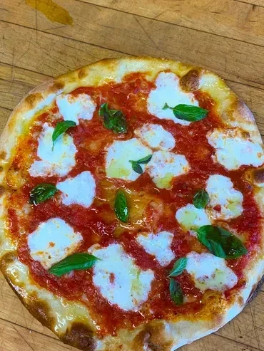 Baked Margherita pizza with tomato, mozzarella, and basil on wood.