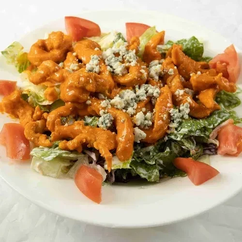 A white plate of buffalo chicken salad with blue cheese and tomatoes.